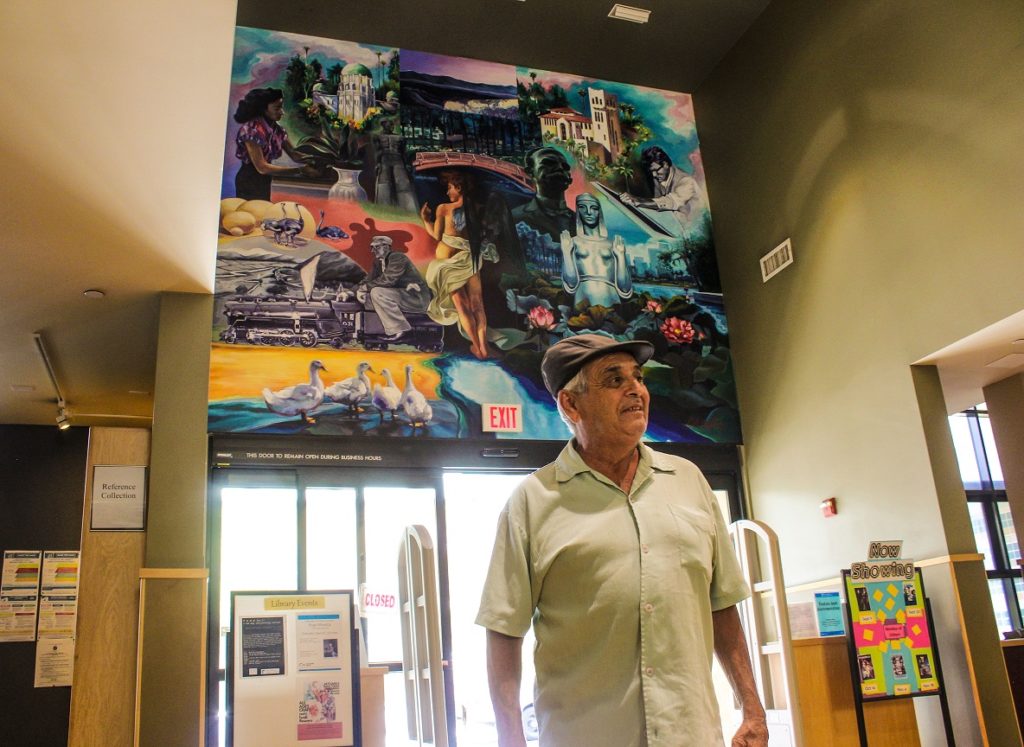 Ernesto De La Rosa stands in front of the mural he painted at the Los Angeles Public Library